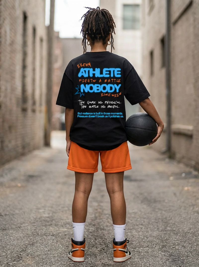 Person wearing a black t-shirt with text and orange shorts holding a basketball in an alley.