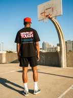 Person wearing a black t-shirt with text and graphics, standing on a basketball court with a clear blue sky.
