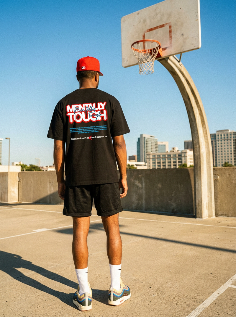 Person wearing a black t-shirt with text and graphics, standing on a basketball court with a clear blue sky.