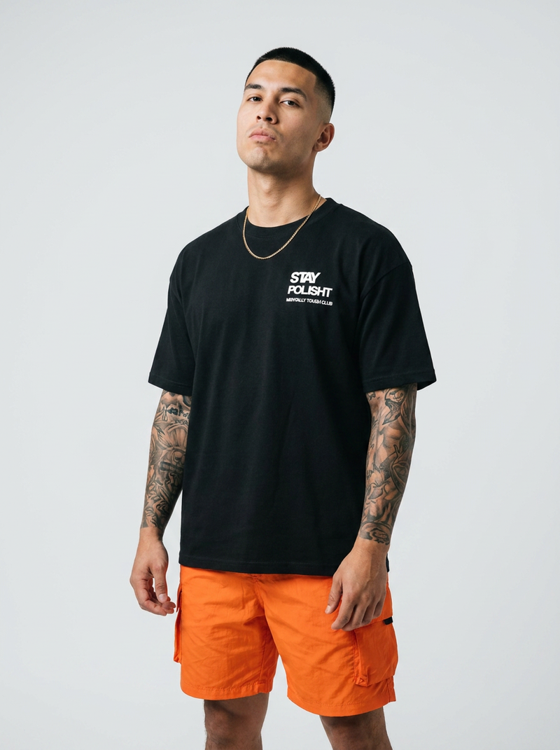Man wearing a black t-shirt with a logo and orange shorts on a white background